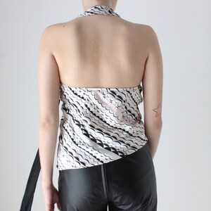 May include: A white halter top with a black and pink abstract print. The top has a tie closure at the back of the neck.