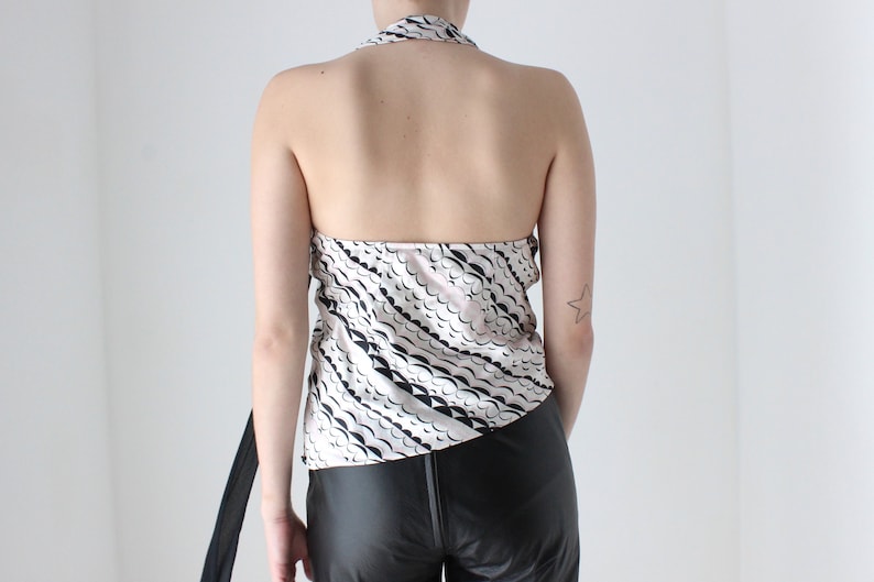 May include: A white halter top with a black and pink abstract print. The top has a tie closure at the back of the neck.