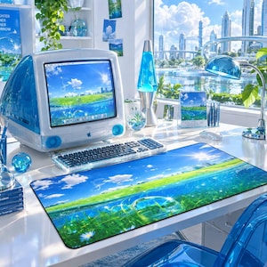 Puede incluir: Un ordenador de sobremesa azul translúcido con teclado a juego y una alfombrilla de escritorio rectangular con un paisaje de campo verde y cielo azul. El conjunto incluye una lámpara de lava azul, una lámpara de escritorio y un portalápices.