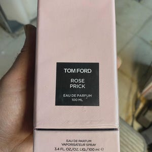 May include: A light pink perfume box with the text "TOM FORD ROSE PRICK EAU DE PARFUM 100 ML". The box also states "3.4 FL. OZ./OZ. LIQ./100 ml e".