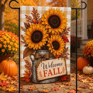 Puede incluir: Una bandera de jardín rectangular con un fondo de cuadros beige y blanco. El diseño muestra una jarra de metal galvanizado llena de girasoles amarillos, bayas naranjas y hojas de otoño, con un letrero que dice Welcome FALL.
