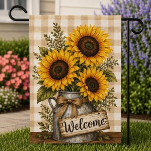 Può includere: Una bandiera da giardino presenta un bouquet di girasoli in un vaso di metallo zincato con un fiocco di juta. La bandiera ha uno sfondo a scacchi beige e bianco e un cartello di legno con la scritta "Welcome".