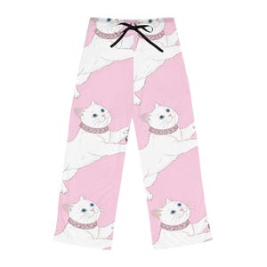 May include: Pink pajama pants featuring a repeating pattern of white cats with blue eyes and pink jeweled collars. The cats are in various poses against a pink background. The pants have a black drawstring at the waist.