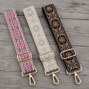 Puede incluir: Tres correas ajustables para bolso con intrincados patrones tejidos. La correa de la izquierda es rosa con motivos florales, la central es gris claro con sutiles diseños geométricos y la de la derecha es negra con patrones florales marrones y blancos, todas con herrajes dorados.