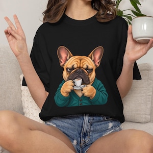 Peut inclure: Un t-shirt noir avec une illustration graphique d'un bouledogue français beige à l'expression grincheuse, portant un gilet boutonné bleu sarcelle et tenant une petite tasse à expresso blanche avec sa soucoupe, centré sur le devant.