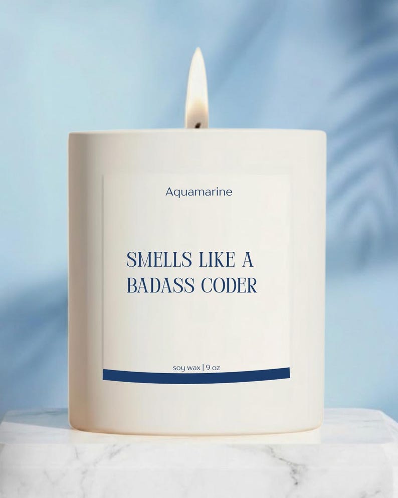 Pode incluir: Uma vela branca acesa com o texto "Aquamarine" e "Smells Like a Badass Coder" em azul marinho. A vela &eacute; feita de cera de soja e pesa 255 gramas. A vela est&aacute; sobre uma superf&iacute;cie de m&aacute;rmore branco contra um fundo azul claro.