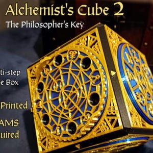 Könnte beinhalten: Der "Alchemist's Cube 2", eine mehrstufige Puzzlebox, zeigt goldene und blaue geometrische Muster. Der Text enthält "The Philosopher's Key" und "100% Printed". Ein einzigartiges dekoratives Objekt.