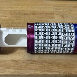 May include: A cylindrical puzzle box with a rotating alphabet cipher. The box is primarily white, with blue and purple accents. The cipher has letters in a grid, and the box is partially open, revealing an interior compartment.