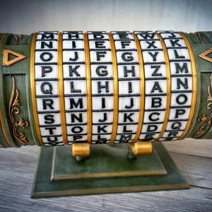 Puede incluir: Un cilindro de cifrado verde y dorado con anillos giratorios con letras. El dispositivo tiene una base rectangular y detalles dorados decorativos. Las letras son negras sobre bloques blancos. El diseño general sugiere un rompecabezas o código secreto.