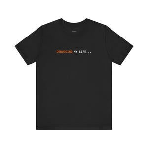 Könnte beinhalten: Schwarzes T-Shirt mit dem Text "DEBUGGING MY LIFE..." in Orange und Weiß. Das T-Shirt hat kurze Ärmel und einen Rundhalsausschnitt. Der Text ist in einer einfachen, serifenlosen Schriftart gehalten.