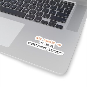 Może przedstawiać: Biała naklejka z napisem "git commit -m 'I HAVE COMMITMENT ISSUES'" w kolorze pomarańczowym i czarnym, umieszczona na laptopie. Klawiatura laptopa jest widoczna w tle.