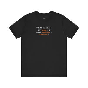 Puede incluir: Una camiseta negra de manga corta con texto en blanco y naranja que dice: UPDATE developer SET sleep = 0 WHERE deadline = 'tomorrow'; El gráfico está centrado en el pecho de la camiseta, que tiene un cuello redondo y un corte estándar.