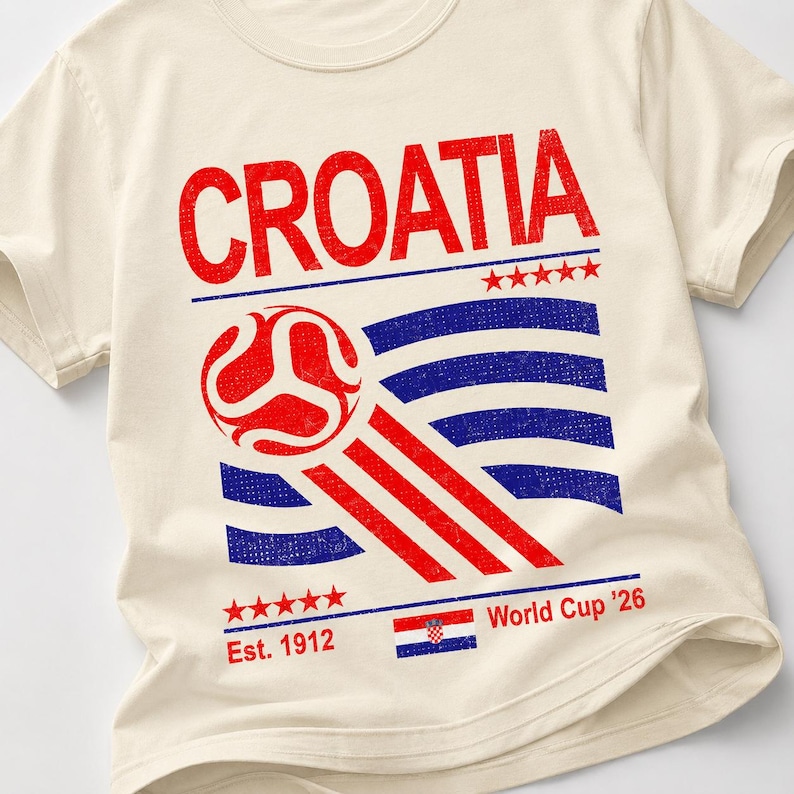 May include: A cream-coloured t-shirt featuring the red text CROATIA at the top. Below is a red soccer ball graphic with motion lines over blue horizontal stripes. The design includes five red stars, the text Est. 1912, a small Croatian flag, and World Cup '26.