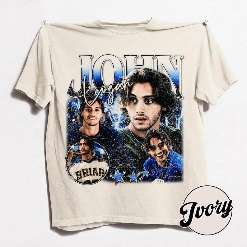 May include: Ivory-colored t-shirt featuring a graphic design with the name "John Logan" in a vintage style. The design includes multiple images of a person, blue stars, and the word "Briar" in a circle.