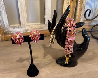 May include: A set of jewelry featuring two cluster earrings and a matching bracelet. The earrings and bracelet are crafted with pink faceted rhinestones and smooth pink cabochon stones set in a gold-tone metal frame, creating a cohesive look.