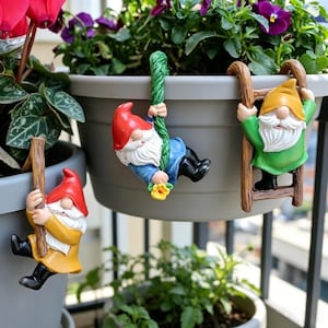 May include: Three garden gnome figurines in various poses. One gnome is climbing a wooden ladder, another is swinging on a green rope, and the third is climbing a wooden pole. Each gnome has a red hat, white beard, and colorful clothing.