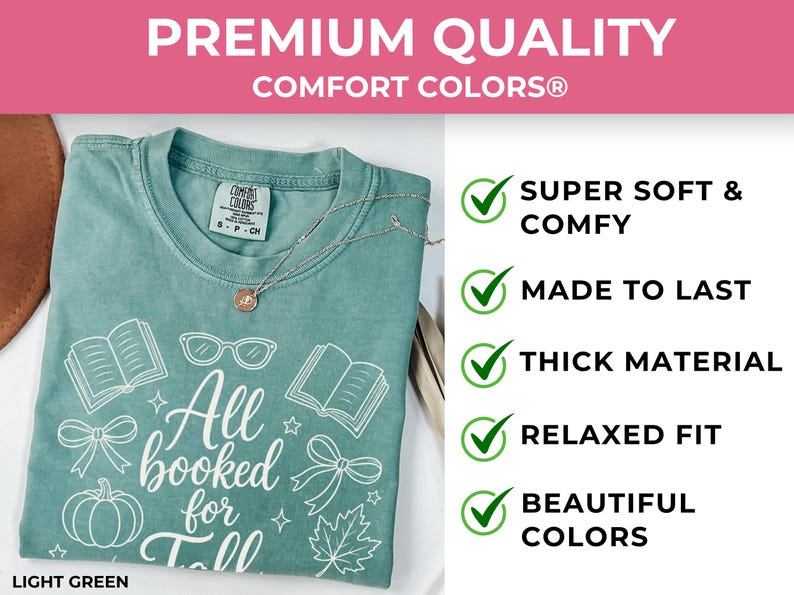 May include: A light green Comfort Colors t-shirt featuring white line art of books, glasses, bows, a pumpkin, and a maple leaf with the text All booked for Fall. The shirt includes a Comfort Colors brand tag and a delicate gold-toned necklace.