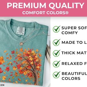 May include: A light green Comfort Colors t-shirt featuring a graphic of a tree with orange, red, and yellow autumn leaves blowing in the wind. The shirt includes text stating Premium Quality, Super Soft & Comfy, Made to Last, Thick Material, Relaxed Fit, and Beautiful Colors.