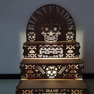 Puede incluir: Un expositor de madera de tres niveles con diseños cortados a láser de calaveras y motivos florales. El arco superior muestra la palabra BIENVENIDOS y el nivel inferior presenta el texto DIA DE MUERTOS. La estructura tiene luz de fondo cálida.