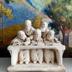 Könnte beinhalten: Eine cremefarbene Skulptur, die fünf bärtige Männer mit Kopfbedeckungen darstellt, die an einem langen Tisch sitzen und in offenen Büchern lesen. Die Figuren sind in einem einfarbigen, strukturierten Stil gehalten und zeigen detaillierte Gesichtszüge.