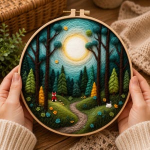 May include: A handmade embroidery hoop art piece featuring a forest scene. The artwork depicts a path winding through a forest with trees, a sun, and a fox. The embroidery is in shades of green, blue, yellow, and brown, with a wooden hoop.