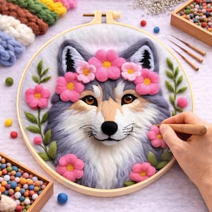 May include: A detailed textile art piece featuring a wolf with gray and white fur, adorned with a pink flower crown and blossoms. The artwork is set in a wooden embroidery hoop, with green leaves and a black nose. Craft supplies are visible.