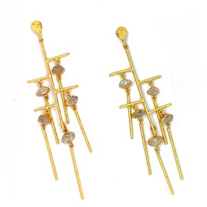 May include: A pair of long gold-tone earrings featuring a textured, branch-like structure with multiple vertical and horizontal bars. Each earring is adorned with several small, clear, irregular-shaped stones suspended from the metal framework.