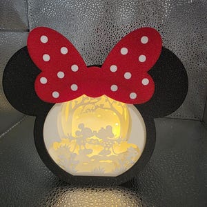 May include: A black Minnie Mouse-shaped light-up decoration with a red bow featuring white polka dots. The interior showcases a silhouette scene of Mickey and Minnie Mouse with the word "Love".