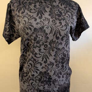 May include: A short-sleeved t-shirt featuring a dark gray and black floral damask pattern. The shirt has a crew neckline and a standard fit. The number 8 is visible in the top left corner, and the letter S is visible in the bottom right corner.
