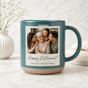 May include: A teal ceramic mug with a speckled finish and a light tan base. The front features a square photo of four people with the printed text "Happy Retirement" and "Love, The Johnson Family" below the image in a script and serif font.