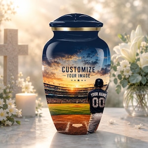 May include: A dark blue cremation urn featuring a printed scene of a baseball stadium at sunset. The text CUSTOMIZE YOUR IMAGE is centered above a baseball player wearing a jersey with the number 00. The urn has a gold-toned metal rim.