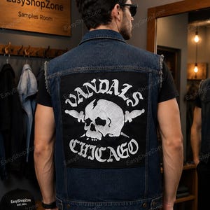 Puede incluir: Un chaleco de mezclilla azul oscuro con un gran parche rectangular negro en la espalda. El parche muestra un gr&aacute;fico blanco de una calavera con dos cuchillos cruzados y el texto VANDALS CHICAGO en una fuente llamativa. El chaleco tiene sisas deshilachadas.