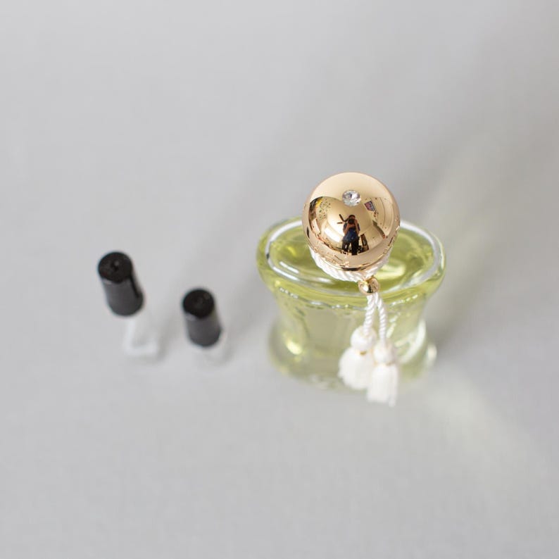 May include: A small, clear glass perfume bottle with a gold-coloured spherical cap. The cap has a small crystal and a white tassel. Two black caps are next to the bottle.