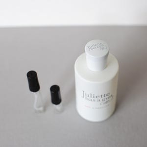 May include: A white perfume bottle with the text "Juliette has a gun" and two small sample vials with black caps. The bottle has a white cap with the brand name printed on it.