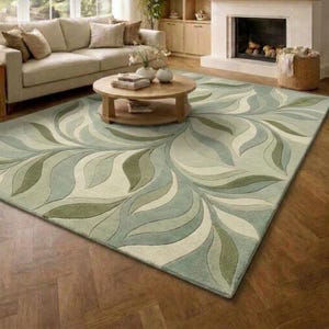 May include: A large rectangular area rug featuring a repeating organic leaf pattern in shades of sage green, olive, and cream. The rug has a soft, tufted texture and covers a significant portion of the dark brown herringbone wood floor.