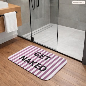 Op de afbeelding: Een rechthoekige badmat met een patroon van verticale paarse en witte strepen. De tekst "GET NAKED" is in vetgedrukte, zwarte, schreefloze hoofdletters in het midden van de mat gedrukt, horizontaal georiënteerd op de vloer.
