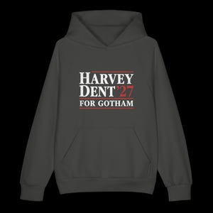 May include: Dark gray hoodie with a front pocket and a hood. The front of the hoodie features the text "HARVEY DENT '27 FOR GOTHAM" in white and red lettering.