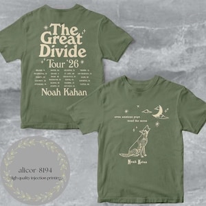 May include: An olive green short-sleeve t-shirt featuring a front graphic of a howling dog, a crescent moon, stars, and the text "even anxious pups need the moon". The back displays "The Great Divide Tour '26" with a list of tour cities.