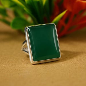 Könnte beinhalten: Ein silberner Ring mit einem großen, rechteckigen, glatten, dunkelgrünen Stein in einer polierten Metallfassung. Der Stein hat eine flache Oberfläche mit abgeschrägten Kanten, und die Ringschiene besteht aus einer einfachen, dünnen Metallstruktur.