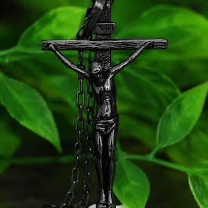 May include: A black metal crucifix pendant featuring a detailed figure of Jesus on a textured cross with the letters INRI inscribed at the top. The pendant is attached to a matching black metal chain link necklace, showcasing a dark finish.
