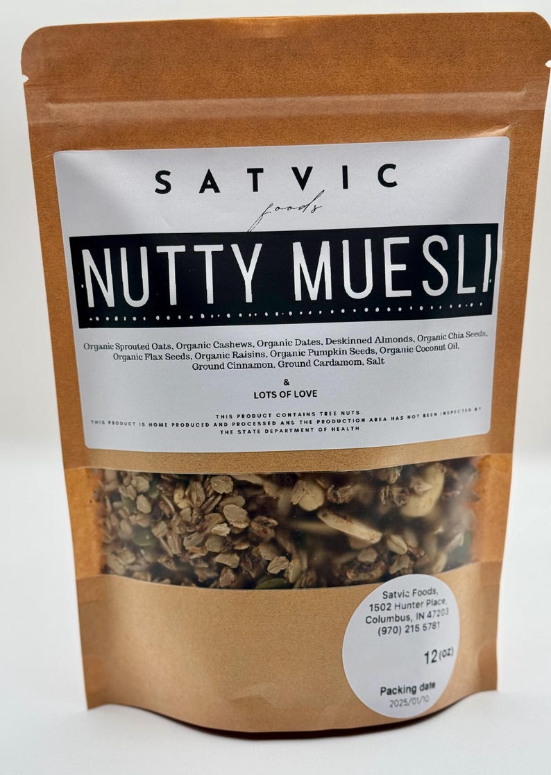 May include: A brown paper bag of "NUTTY MUESLI" from Satvic Foods. The bag features a clear window showing the granola mix of oats, nuts, seeds, and spices. The label lists ingredients and the words "& LOTS OF LOVE."