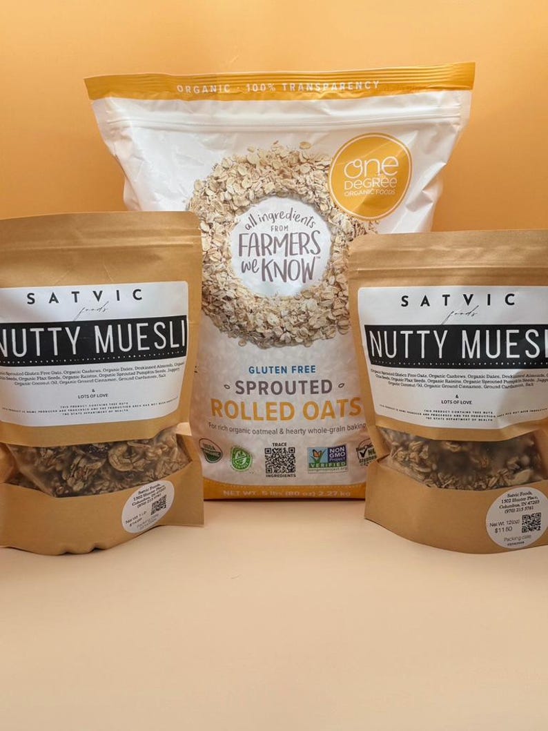 May include: An assortment of organic oat products, including bags of "Nutty Muesli" and "Sprouted Rolled Oats." The packaging features text such as "Gluten Free" and "Lots of Love." The background is a solid orange color.