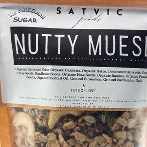 May include: A bag of "Nutty Muesli" from Satvic Foods, with a clear window showing the mix of oats, nuts, seeds, and dried fruit. The label states "No Additional Sugar" and lists ingredients like cashews, dates, and coconut oil.
