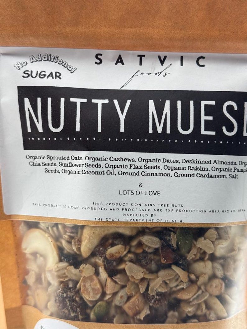 May include: A bag of "Nutty Muesli" from Satvic Foods, with a clear window showing the mix of oats, nuts, seeds, and dried fruit. The label states "No Additional Sugar" and lists ingredients like cashews, dates, and coconut oil.