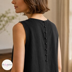 May include: Black sleeveless dress with a row of small, round buttons down the back. The dress has a simple, elegant design and appears to be made of a lightweight fabric. The back of the dress is the focus of the image.