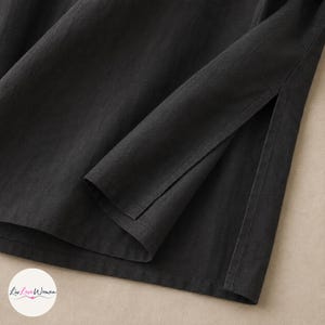 May include: Close-up of a black garment with a long sleeve and a side slit. The fabric appears to be a soft, woven material. The garment is likely a top or dress.