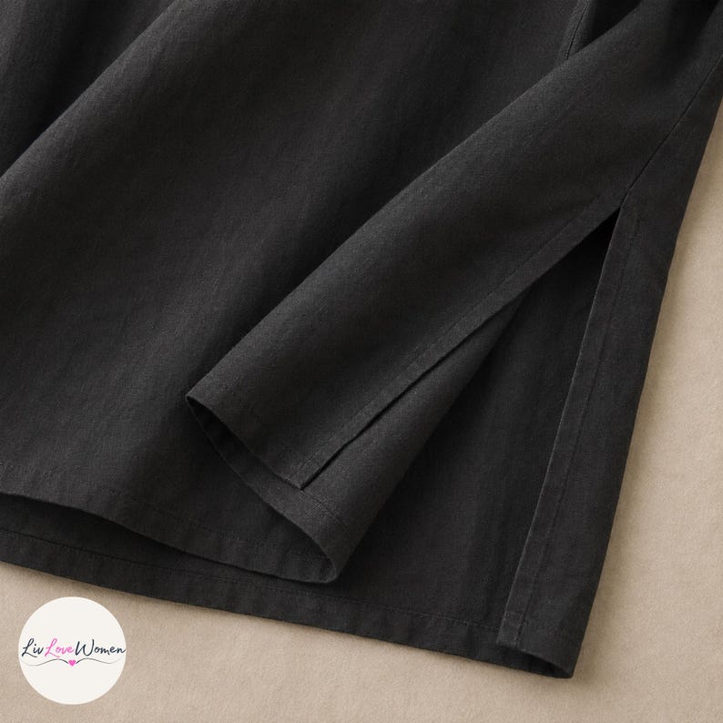 May include: Close-up of a black garment with a long sleeve and a side slit. The fabric appears to be a soft, woven material. The garment is likely a top or dress.