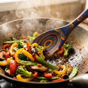 Puede incluir: Un wok lleno de coloridas verduras salteadas, que incluyen pimientos rojos y amarillos, br&oacute;coli y guisantes. Una cuchara de madera con un dise&ntilde;o vibrante de c&iacute;rculos conc&eacute;ntricos revuelve la comida, con vapor saliendo de la sart&eacute;n.