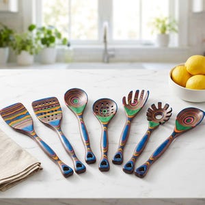 Puede incluir: Un juego de siete utensilios de cocina de madera coloridos, que incluyen una esp&aacute;tula, una cuchara ranurada y una cuchara para servir. Los utensilios tienen mangos azules y est&aacute;n colocados sobre una encimera blanca junto a un pa&ntilde;o de lino y un cuenco de limones.
