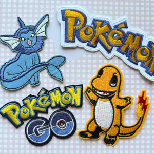 May include: Embroidered patches featuring characters and logos from the Pokémon franchise. Includes a blue Vaporeon, an orange Charmander, and multiple Pokémon logos in yellow and blue. The patches are on a pink and white checkered background.